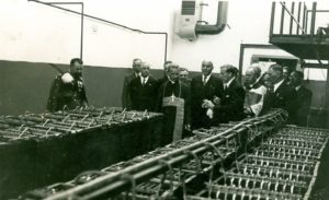Fotografia uroczystości w fabryce z ok 1937 r., grupa osób zwiedzających pomieszczenia zakładu